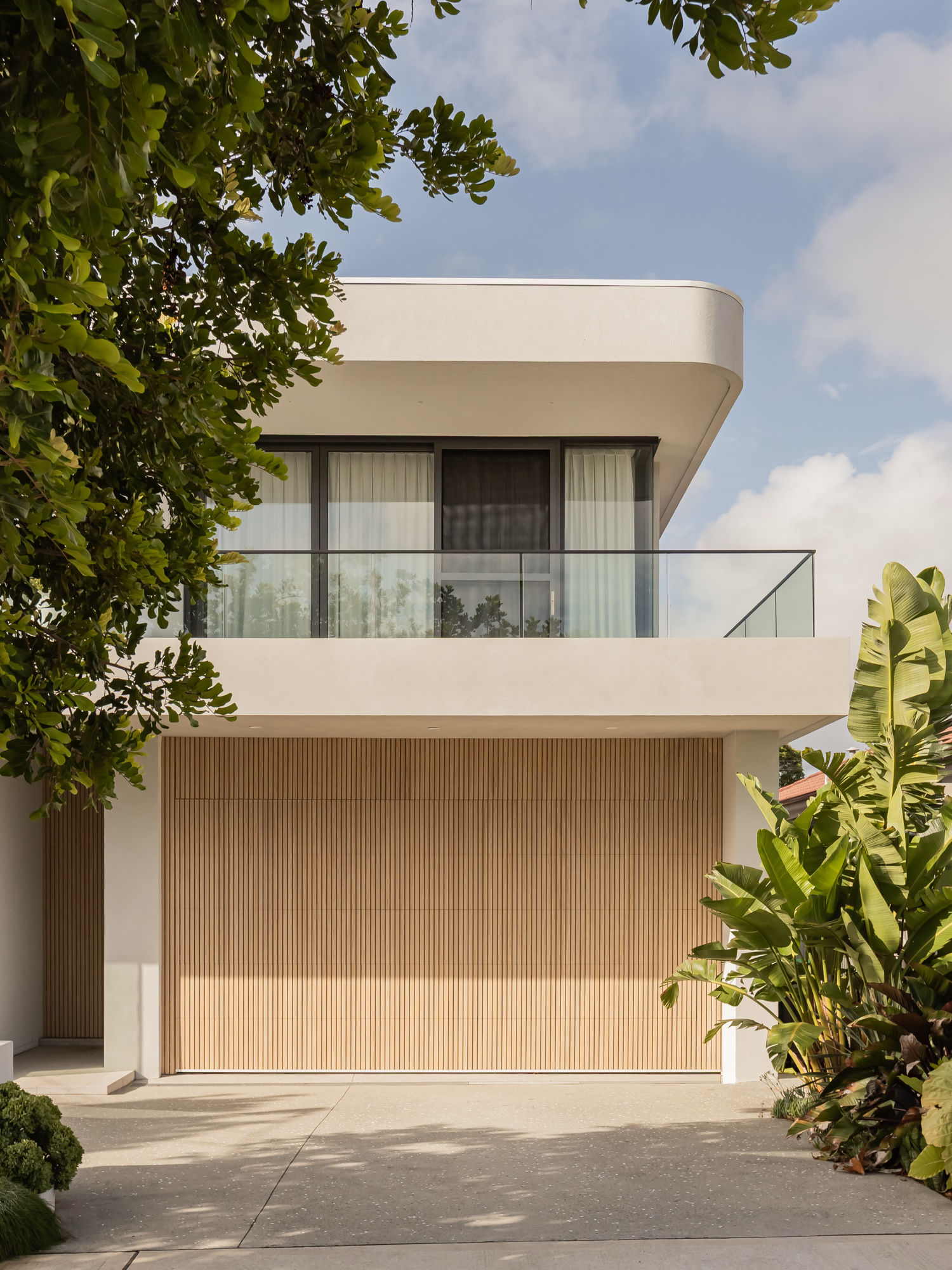 Curved rendered upper level above a battened timber garage, framed by planting