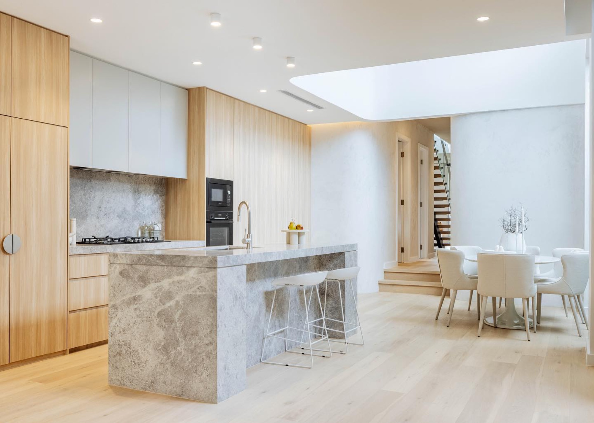Oak kitchen with grey marble island, dining and stair beyond, lit by a long skylight