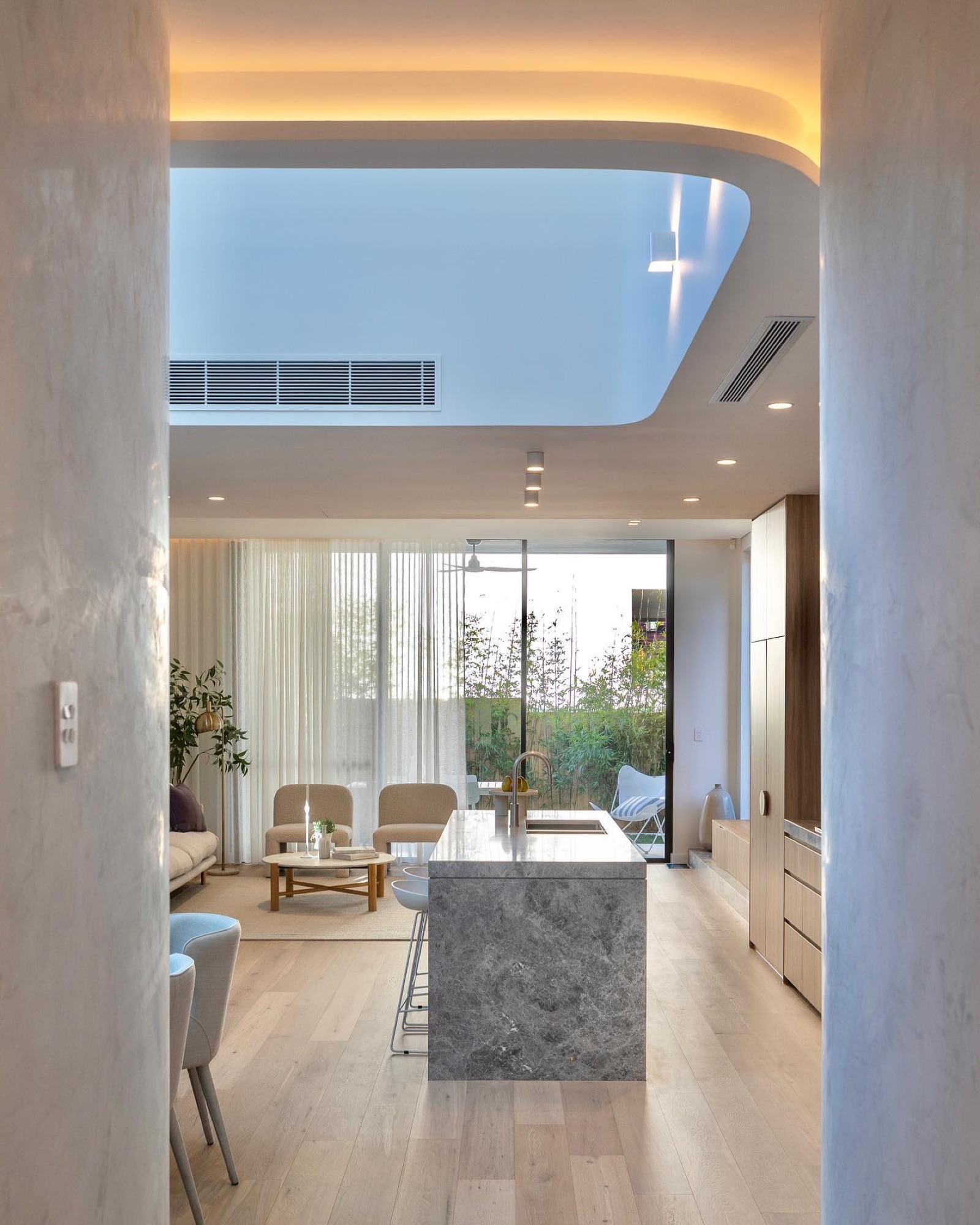 Curved ceiling with cove lighting over the kitchen island, living room beyond